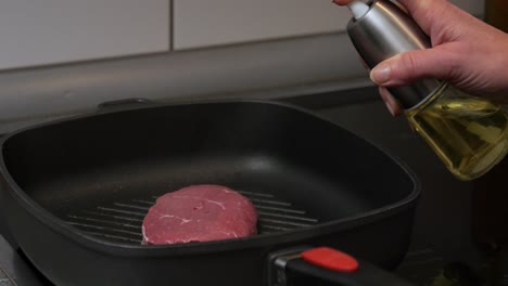 Close-up-shot-of-a-woman-using-an-oil-sprayer-to-fry-a-beef-steak-in-a-hot-pan-with-olive-oil-while-preparing-a-delicious-dinner
