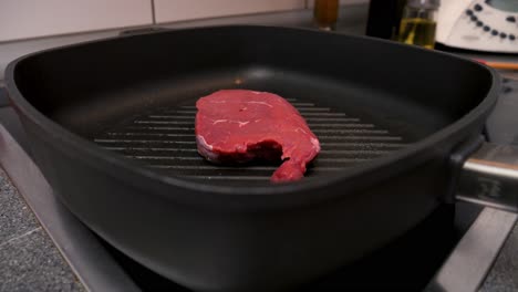 Close-up-shot-of-a-delicious-steak-in-the-hot-pan-during-searing-in-a-kitchen-in-slow-motion