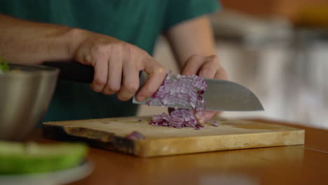 Close-up-man-cutting-onion-on-wooden-board,-filmed-in-slow-motion