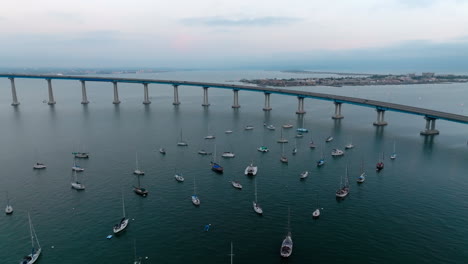 Cinematic-drone-shot-of-small-yachts-and-sail-boats-parked-near-curved-Coronado-bridge-in-San-Diego,-California
