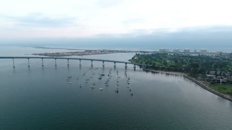 Aerial-panning-shot-above-the-San-Diego-bay,-Coronado-Island-Marina-near-beautiful-curved-bridge-in-the-background