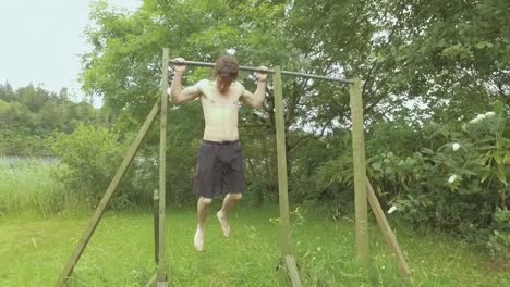 Young-fit-man-doing-behind-neck-pullups-outdoors-surrounded-by-nature