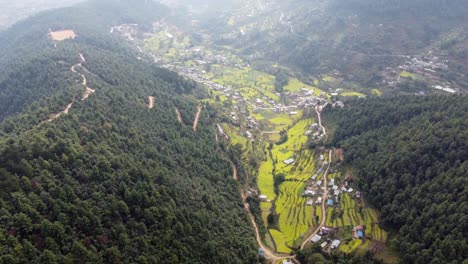 Eine-Wunderschöne-Luftaufnahme-Der-Vorberge-Des-Himalaya-Mit-Einer-Straße,-Die-Sich-Entlang-Des-Fußes-Eines-Hügels-Mit-Verstreuten-Senffeldern-Und-Häusern-Windet