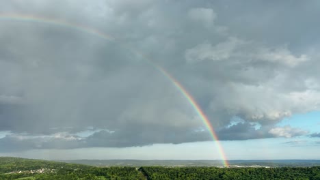 Eine-Nach-Links-Schwenkende-Luftaufnahme-Eines-Regenbogens-Nach-Einem-Gewitter-über-Der-Wunderschönen-Grünen-Landschaft