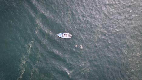 Aufsteigende-Drohnenaufnahme-Eines-Fischerbootes-Im-Ozean-Mit-Schwimmenden-Menschen