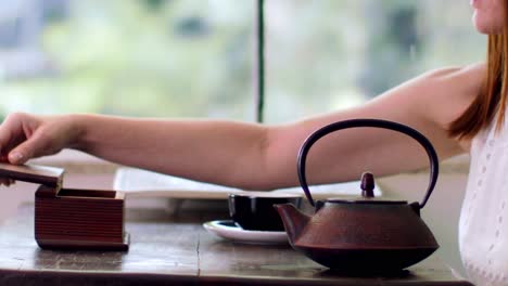 Woman's-hand-seen-pouring-hot-water-infused-with-organic-herbal-tea-from-a-vintage-Asian-teapot---isolated-slow-motion