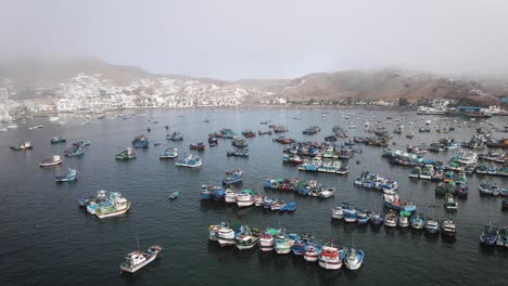 Drone-shot-of-fishing-boats-in-a-fishing-port-next-to-beach-houses-and-yachts-in-the-cost-of-Pucusana-Peru-during-summer