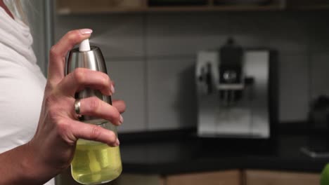 Static-close-up-shot-of-a-woman-with-an-oil-sprayer-in-her-hand-while-spraying-oil-for-cooking-in-the-kitchen-with-a-coffee-machine-in-the-background