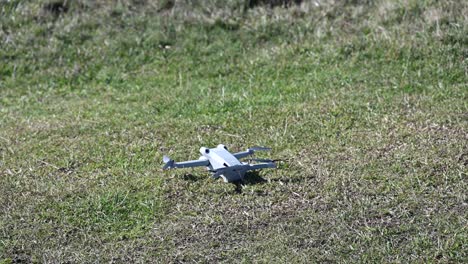 Un-Dron-Aterriza-En-Un-Suelo-De-Hierba,-Equipo-De-Filmación-Con-Hélices