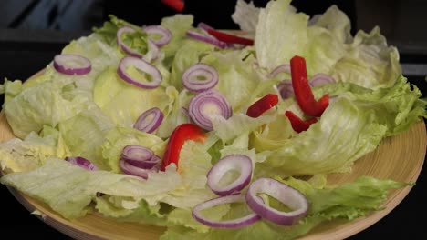 Close-up-handheld-shot-of-preparing-a-delicious-salad-with-onion,-peppers-and-other-vegetables-garnished-by-a-woman's-hand