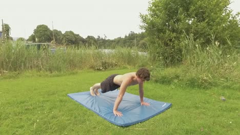 Athletic-young-man-performs-wide-pushups-outdoors-in-garden