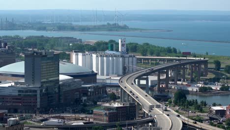 An-time-lapse-aerial-view-of-the-city-of-Buffalo,-New-York-and-its-infrastructure-of-bridges-and-buildings-beside-Lake-Erie-with-some-wind-turbines-in-the-background