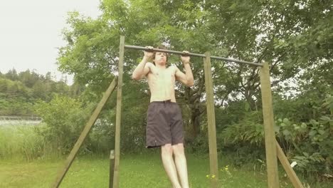 Young-athletic-man-doing-pullups-on-outdoor-home-gym-by-river