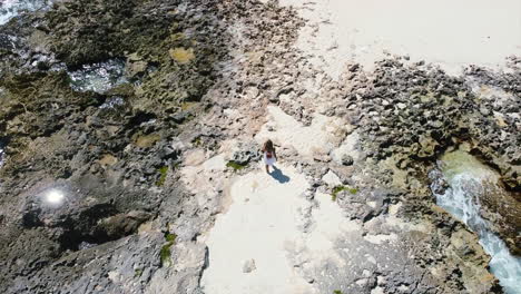 aerial-top-down-of-young-girl-walking-on-rocky-beach-in-Cozumel-Mexico-on-sunny-day