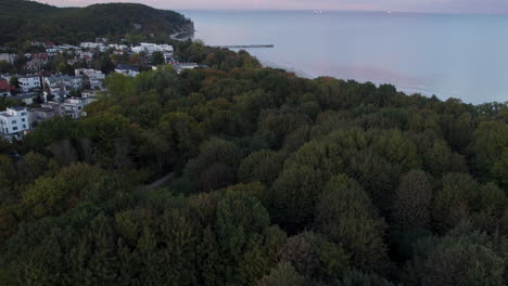 A-subtle-and-cinematic-ascent-above-the-trees-with-a-view-of-the-pier-in-Gdynia-Orłowo---in-the-background,-the-bay-of-Gdańsk-at-sunset-with-ships-on-the-roadstead