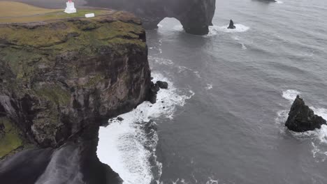 Aerial-of-Dyrhólaey-viewpoint-with-a-lighthouse-at-the-coast-of-Iceland-with-dramatic-cliffs