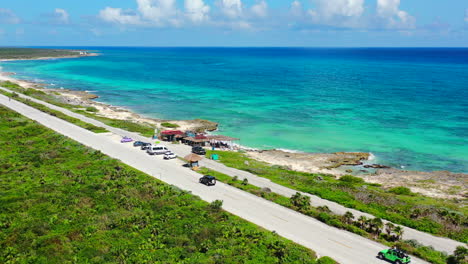 cars-driving-on-coastline-of-Cozumel-Mexico-with-turquoise-water-and-white-sand-beaches-on-summer-day,-aerial