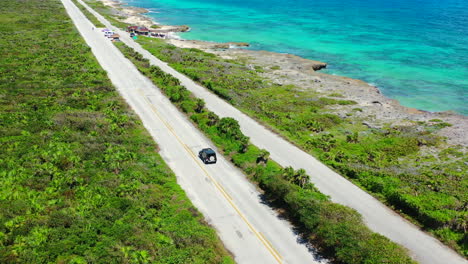 SUV-driving-in-Cozumel-Mexico-with-stunning-turquoise-blue-ocean-coastline,-aerial
