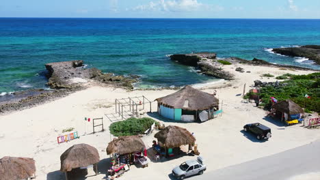 cars-parked-at-beachside-souvenir-shops-on-Cozumel-Island-in-Mexico-overlooking-tropical-turquoise-beach,-aerial