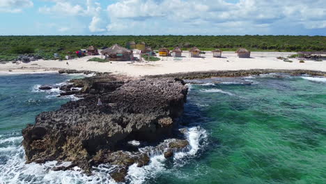 beach-huts-on-rocky-Cozumel-island-beach-with-turquoise-waves-crashing-in-Mexico-on-sunny-day,-aerial