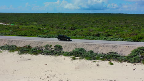 Jeep-driving-on-empty-coastline-road-in-Cozumel-Mexico-on-sunny-day,-aerial