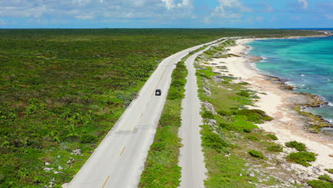 aerial-panoramic-of-lush-green-island-with-car-driving-on-long-oceanside-road-in-Cozumel-Mexico