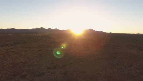 Ascending-drone-shot-of-desert-with-sunsetting-behind-mountain-in-the-background-with-lens-flare-located-in-Flagstaff-Arizona