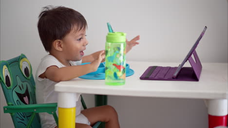 Cute-latin-Toddler-watching-a-movie-on-a-tablet-while-eating-breakfast-sitting-on-a-baby-table