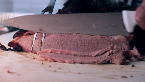 Close-up-shot-of-men-hand-cutting-brisket-above-the-tray