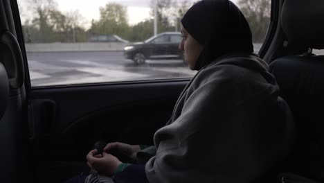 Asiatische-Frau,-Die-Hijab-Trägt,-Im-Auto-Fährt-Und-Durch-Das-Fenster-Schaut
