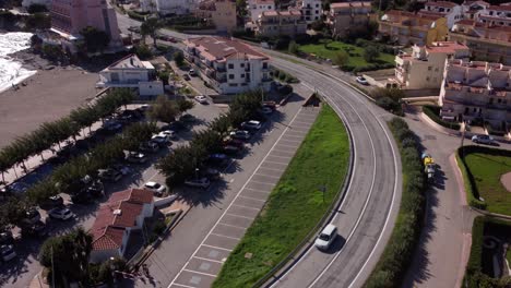 Drone-shot-of-a-white-car-driving-along-a-coastal-road-on-the-Costa-Brava,-in-Catalonia,-Spain