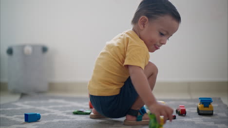 Young-cute-latin-toddler-on-the-floor-on-a-grey-playing-alone-with-his-car-toys-having-fun