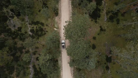 Birds-eye-view-of-a-jeep-driving-through-a-mountain-road-in-the-forest,-aerial-tracking-shot