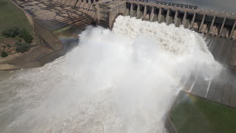 Aerial-flight-to-power-dam-water-release-with-downstream-rainbow