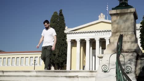 Bearded-man-walks-in-front-of-Athens-Historic-Zappeion-sunny-day-in-white-shirt