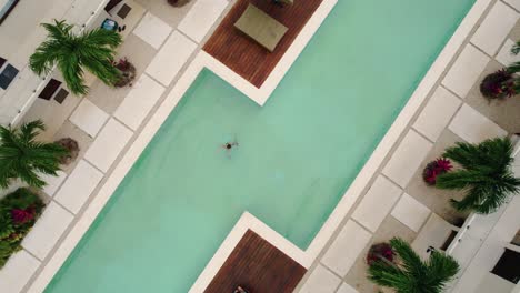 Drohnenaufnahme-Eines-Mädchens,-Das-Im-Pool-Des-Blauen-Luxushotels-Tulum-Schwimmt