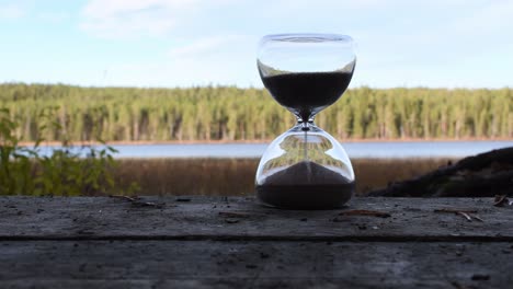 Time-glass-on-the-wooden-surface-with-nature-background