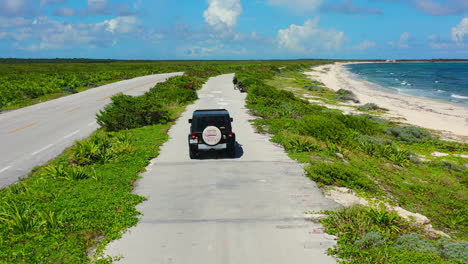 aerial-of-SUV-driving-on-green-island-coastline-with-tropical-white-sand-beach-and-turquoise-water-in-Cozumel-Mexico
