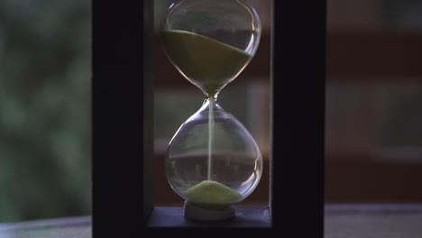 Hourglass-with-yellow-sand-falling-down-on-a-wood-table