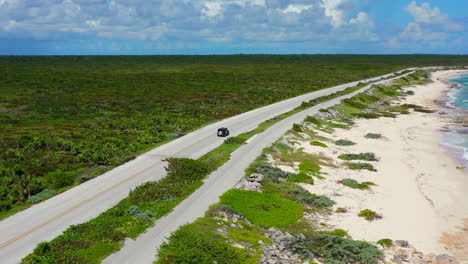 aerial-of-vehicle-driving-on-empty-island-road-with-pristine-white-sand-beaches-on-a-sunny-day