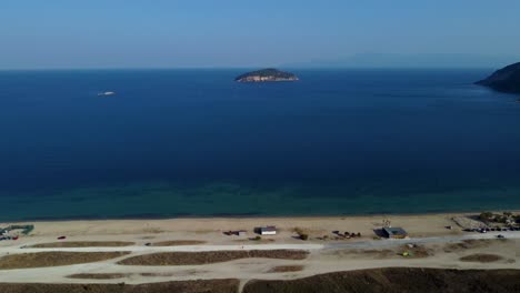 Langsamer-Luftschwenk-über-Strand-Mit-Kleiner-Griechischer-Insel-In-Der-Ferne