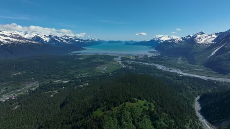 Denso-Bosque-De-Pinos-Y-Tranquilo-Lago-Azul-Entre-Montañas-Nevadas-En-Alaska-En-Un-Día-Soleado
