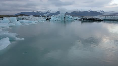 Vista-Posterior-De-Una-Persona-Aislada-E-Irreconocible-Caminando-Hacia-Las-Orillas-Del-Lago-Glaciar-Jokulsarlon-Con-Montañas-En-El-Fondo,-Islandia
