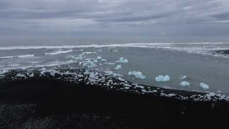 Unrecognizable-people-on-small-icebergs-along-Diamond-beach,-Iceland