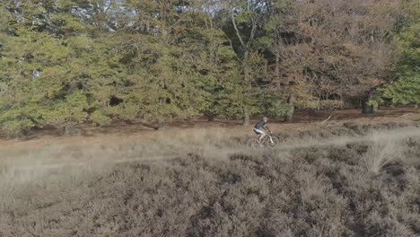 Side-drone-shot-of-a-mountainbiker-riding-uphill-in-nature