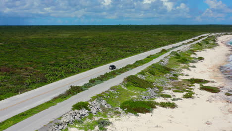 car-driving-on-long-empty-coastline-road-surrounded-by-vast-jungle-in-Cozumel-Mexico