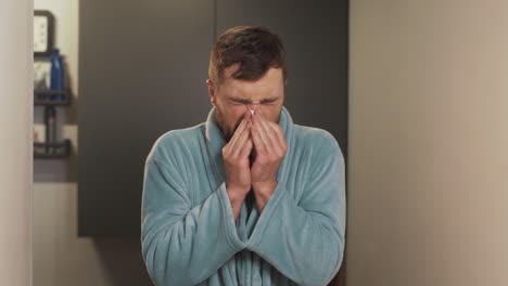 Portrait-of-a-young-man-in-a-bathrobe-sneezes-and-wipes-his-nose-on-a-napkin