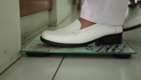 Close-up-of-Woman's-foot-with-white-shoes-On-Scales-Measure-Weight-in-a-clinic
