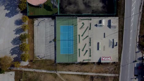 Aerial-top-down-descent-over-outdoor-sports-facilities-with-tennis,-basketball,-mini-golf-and-skate-park
