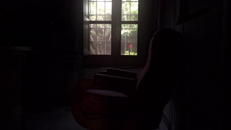 Alter-Sessel-In-Einem-Dunklen-Raum-Vor-Einem-Fenster,-Durch-Das-Das-Licht-Einfällt